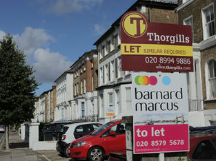 A imagem mostra uma rua residencial em Londres, com placas de "aluga-se" de duas imobiliárias, Thorgills e Barnard Marcus, indicando que há propriedades disponíveis para alugar na área.