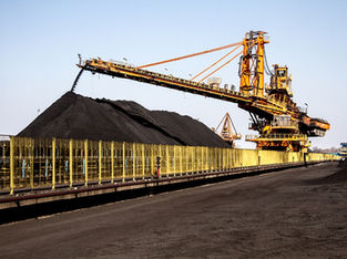 A imagem mostra uma operação de mineração, provavelmente de carvão, com uma grande máquina de empilhamento descarregando o material para formar uma pilha.