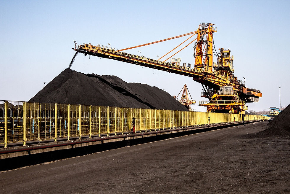 A imagem mostra uma operação de mineração, provavelmente de carvão, com uma grande máquina de empilhamento descarregando o material para formar uma pilha.