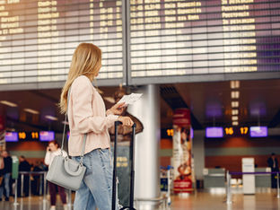 Mulher olha para seu cartão de embarque em mãos dentro de aeroporto