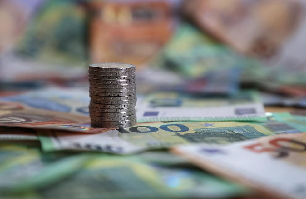 A imagem mostra uma pilha de moedas e várias notas de euro espalhadas, representando a forma física do dinheiro em circulação.