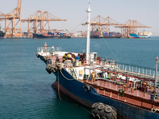 A imagem mostra um navio petroleiro em um porto, com guindastes ao fundo, o que remete ao transporte e comércio de petróleo.