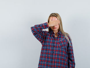 Mulher está com camisa comprida e cobre o rosto com a mão