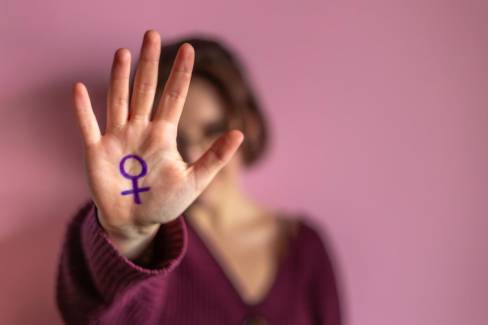 Mulher com suéter roxo exibe a palma da mão voltada para a câmera, com o símbolo do gênero feminino desenhado em roxo.