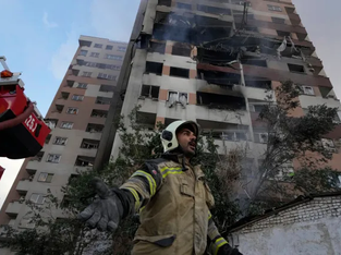 Bombeiro aparece com os braços abertos, ao fundo um prédio bombardeado
