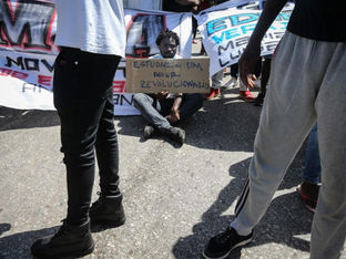 Homem sentado com placa de protesto em mãos