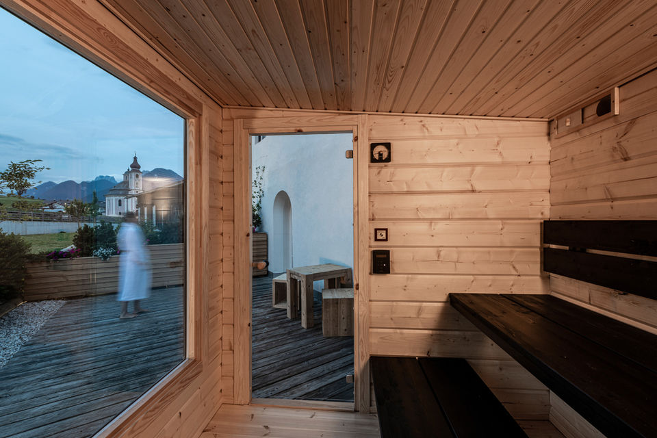 Hetki Sauna interior with black spruce plank benches, view through door and window to outdoor garden from Finnish log sauna.
