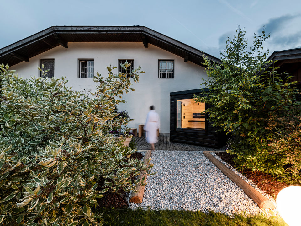 Hetki outdoor Finnish log sauna in hotel garden at dusk with lights on, person entering, evening wellness haven oasis in Finland.