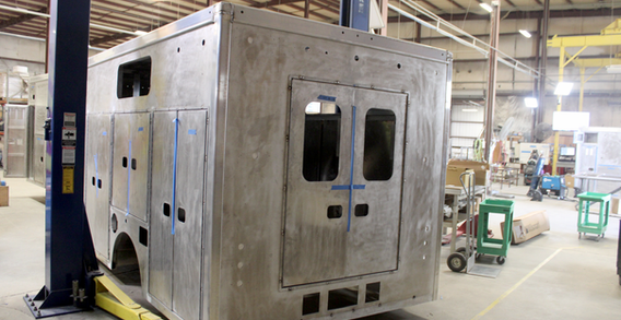 Rear driver side corner view of Rescue truck for Alamosa #2638 from Custom Truck and Body Works, Inc. on welding lift.