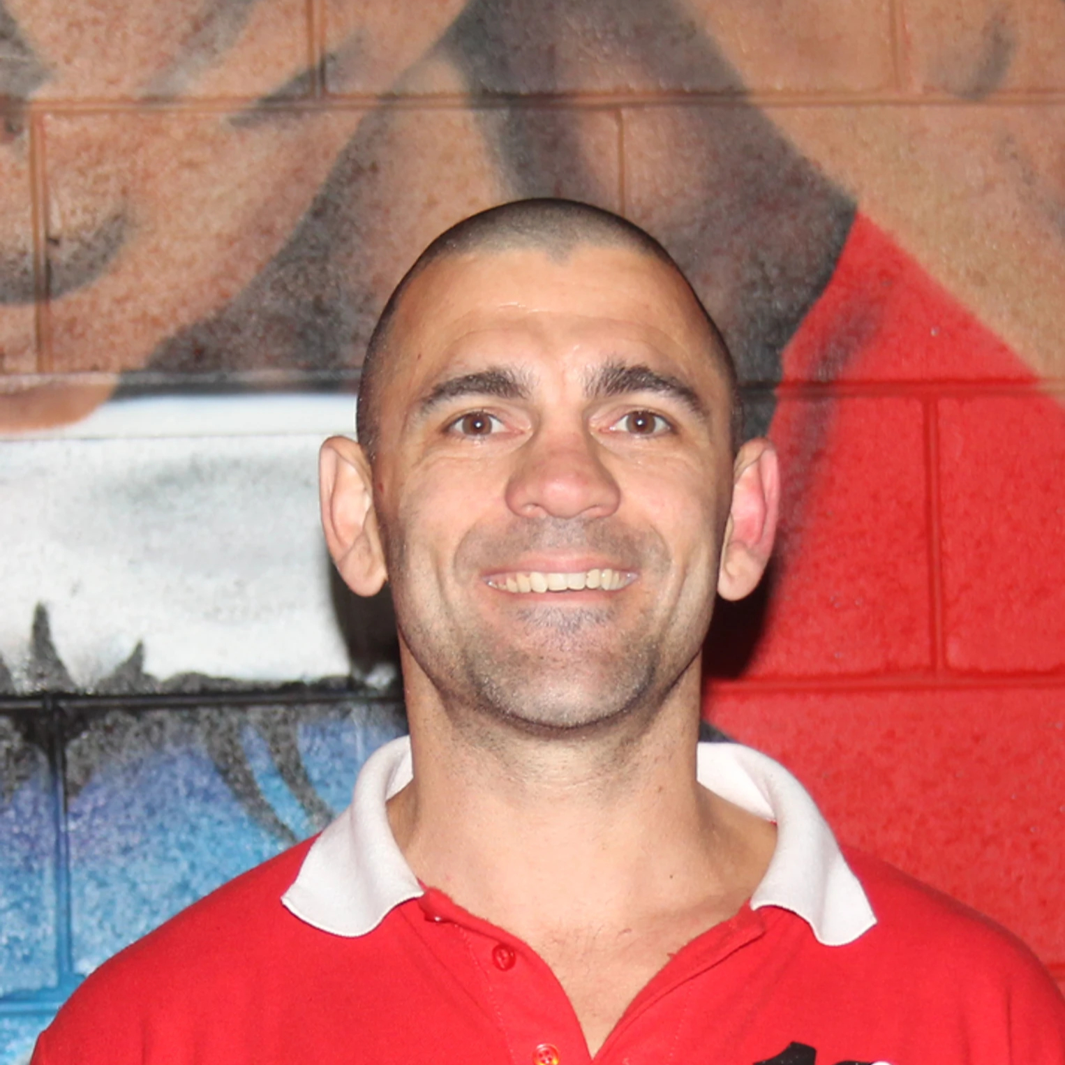 Tim Drury in Fite108 red polo, displaying tattoos, with a colorful mural background.