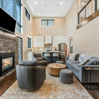 Interior photo of fireplace and furnished living room, brown wood floors and floor to ceiling windows, view of the kitchen