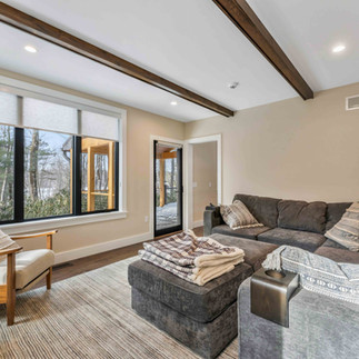 Exposed beams on the ceiling of a smaller living room with a large grey sectional and large windows