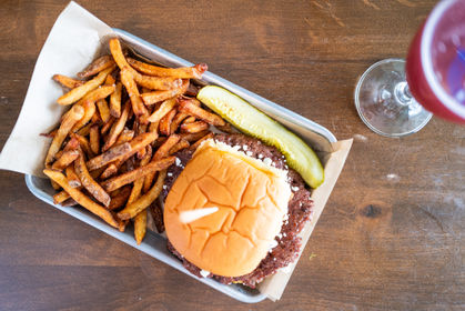 Burger, fries, and pickle on a tray with drink on wooden table