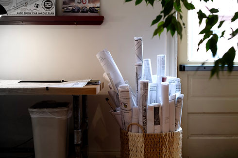 Rolled architectural plans inside a woven basket near a desk and window.
