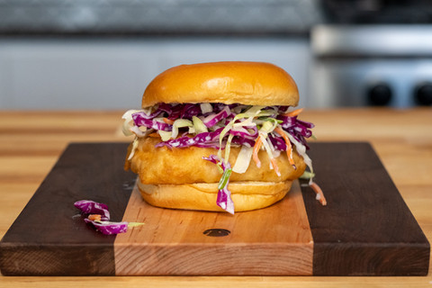 Delicious fish sandwich with coleslaw visible and the ingredients on cutting board.