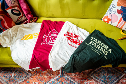 Four t-shirts with different designs on a yellow couch, stay calm industries.