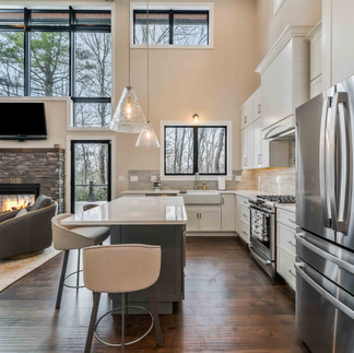 Interior photo of kitchen, white cabinets and beautiful kitchen island, view into living room with floor to ceiling windows