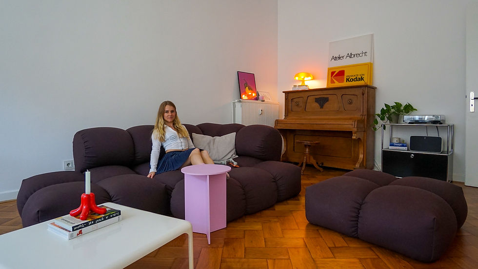 Woman on a dark purple sofa in a cozy living room with glowing lamps, piano, and a Kodak sign.