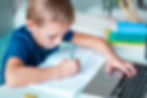 Closeup of little young school boy working at home with a laptop and class notes studying