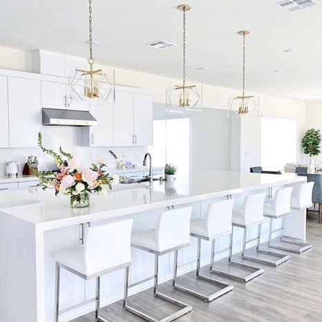 white, modern kitchen with long white island with six chairs on side facing sink
