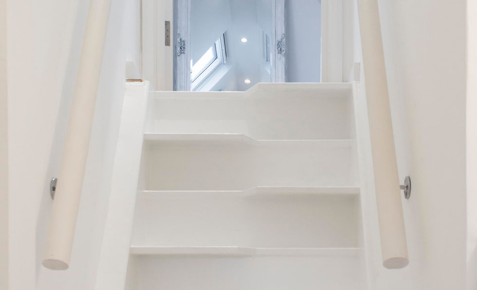 Bright white staircase with a handrail leading to a well-lit attic room with a skylight.

