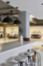 Modern garage interior with luxury cars, bar stools, and pendant lights. Concrete counter with vase and bowl creates a stylish atmosphere.