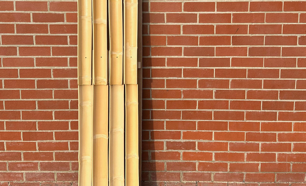 Several long, vertical bamboo panels with a curved top edge are stacked against a red brick wall.