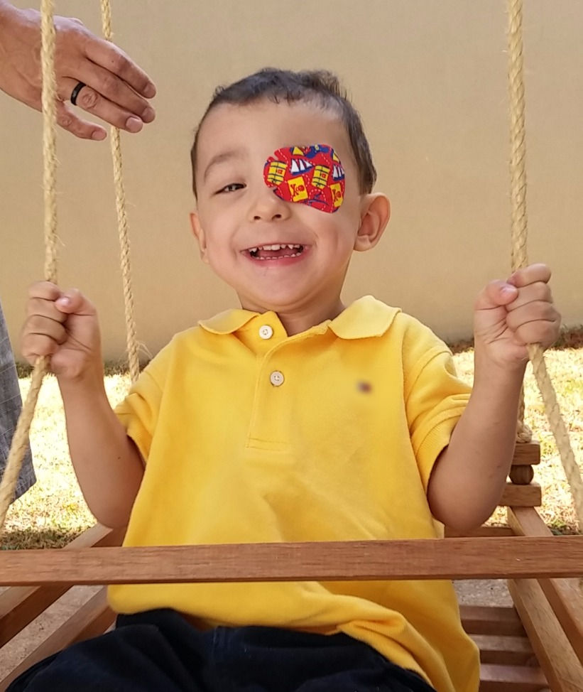 Menino sorridente no balanço com adesivo no olho