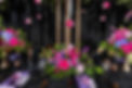 This dramatic tablescape captures the essence of modern romance with rich jewel-toned florals, luxurious black linens, and moody candlelight. Vibrant hues of fuchsia, violet, and sapphire are artfully arranged among lush greenery and suspended blooms, creating a captivating focal point. Accented with black and gold tableware and delicate lavender napkins, this design offers a striking balance of elegance and edge—perfect for couples seeking a bold, unforgettable celebration.