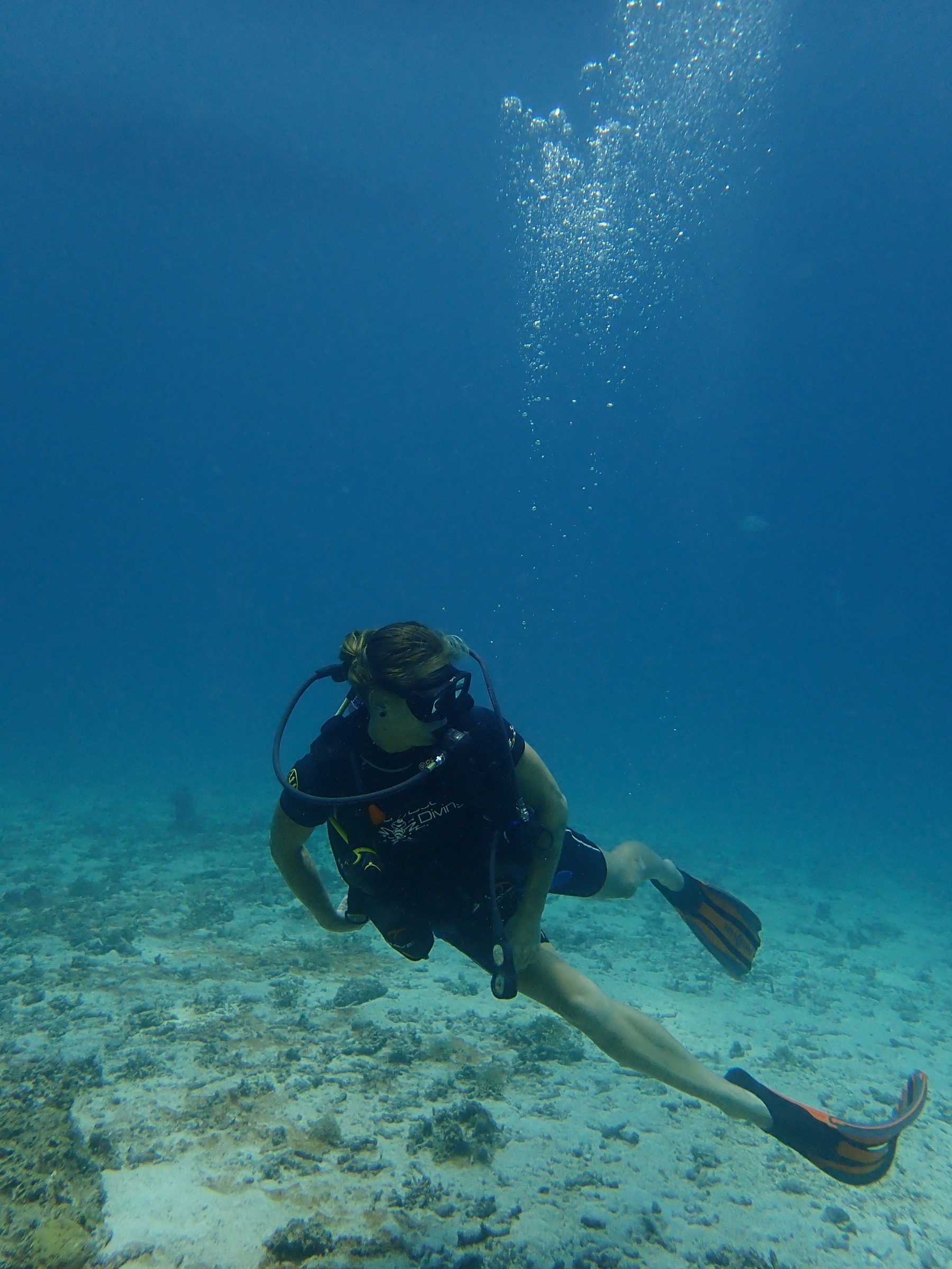 Scuba diver hovering in blue water above a sandy seabed