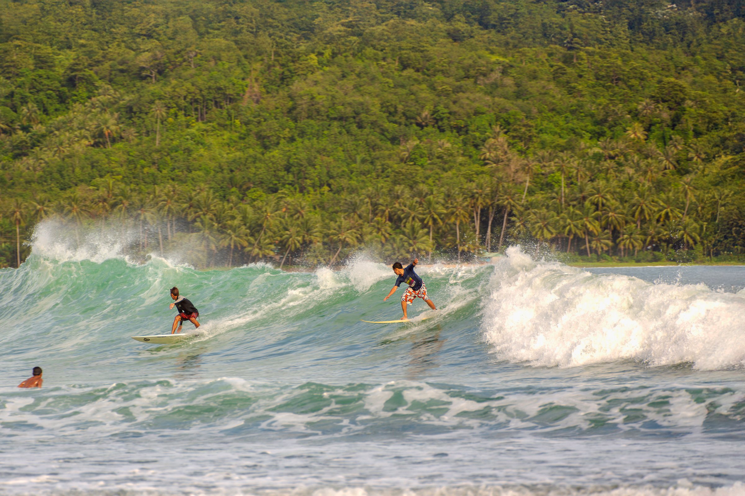 Two surfers riding a wave at Pakarang Beach, Khao Lak