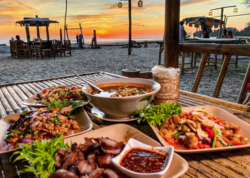 Thai dishes on a beachfront table at sunset