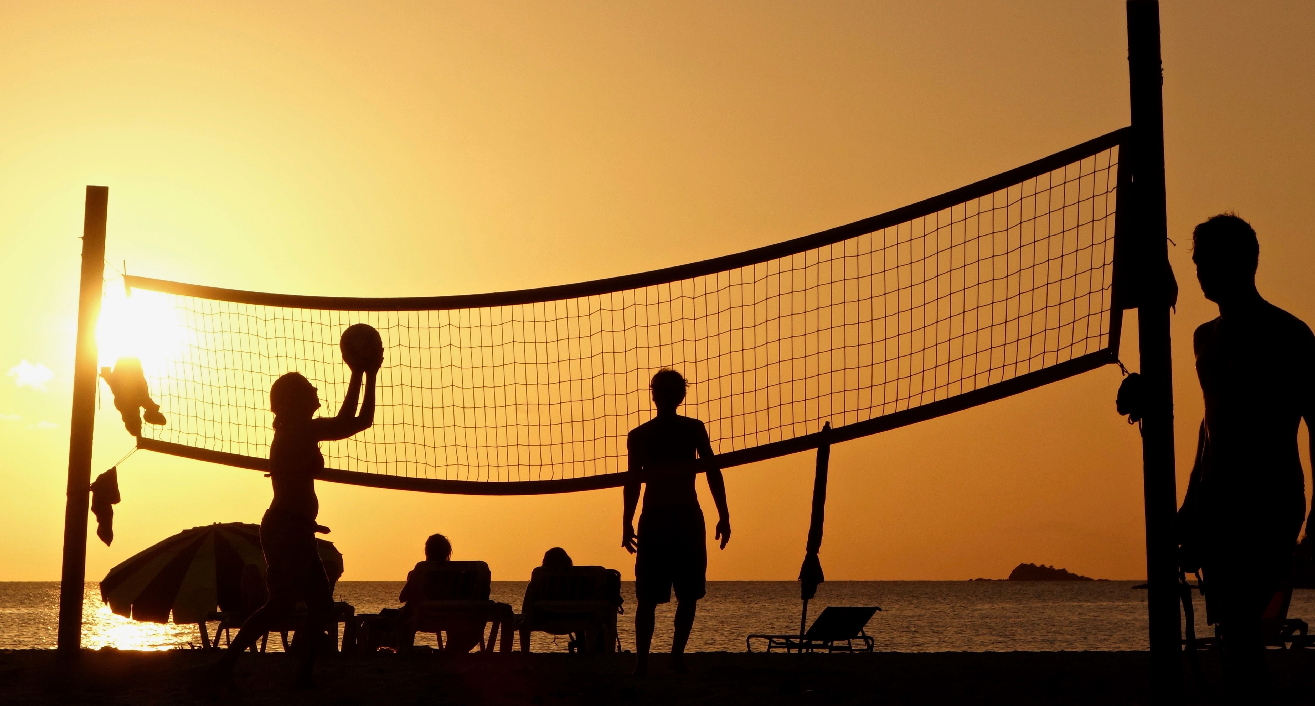 People playing beach volleyball at sunset
