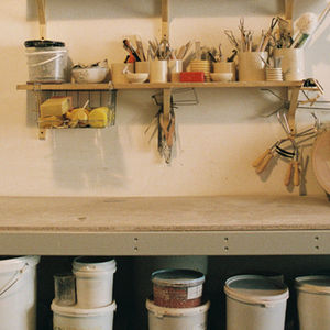 Pottery tools, brushes, and glaze jars on shelves above a workbench at Studio Marvila.