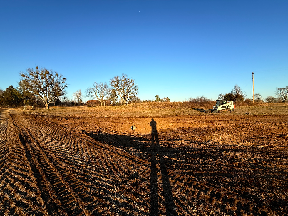 view of cleared land with dozer track marks visible in the ground and a shadow of an operator is cast long from the setting sun