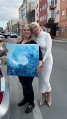 Soledad Reina reina y una cliente lucen sonrientes en la calle sosteniendo una vibrante obra de una ola marina.