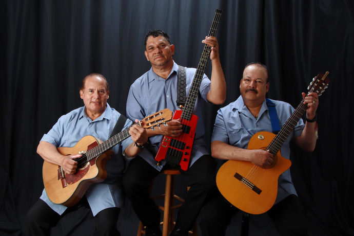 Mariachi trio performing together on stage with string instruments under professional lighting.