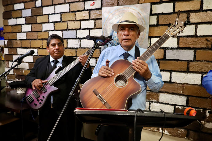 Mariachi guitarrón player performing in front of a brick wall during a live event.