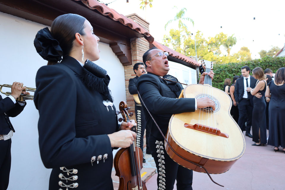 Mariachi musicians performing outdoors in traditional attire during a formal gathering.