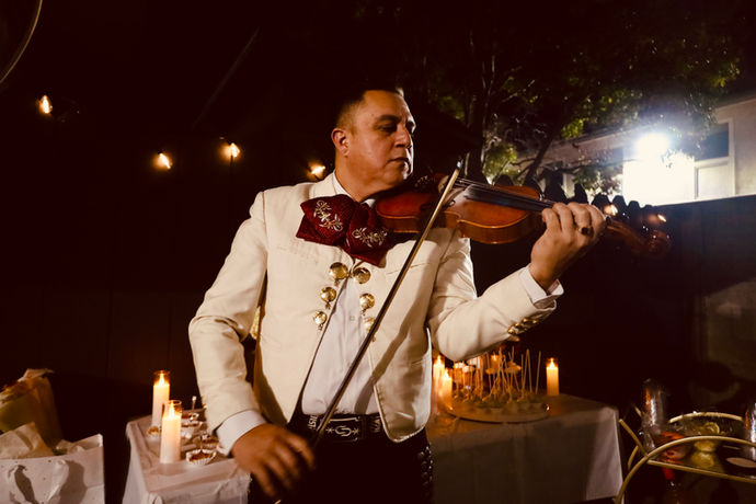 Mariachi violinist performing at an evening outdoor event with candlelight.