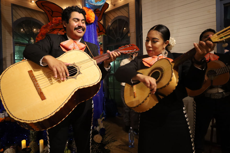 Mariachi musicians performing together indoors, playing guitarrón and guitar at a lively celebration.