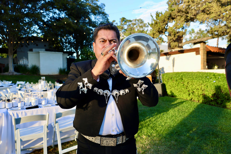 Mariachi trumpet player performing outdoors at an elegant private event with banquet seating.