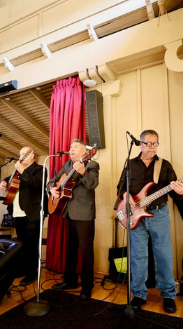 Wide shot of a Latin trio ensemble performing live with guitars and bass at an indoor event.
