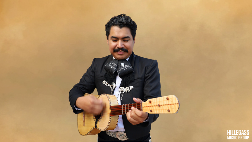 Mariachi musician playing vihuela in a black charro suit against a studio backdrop
