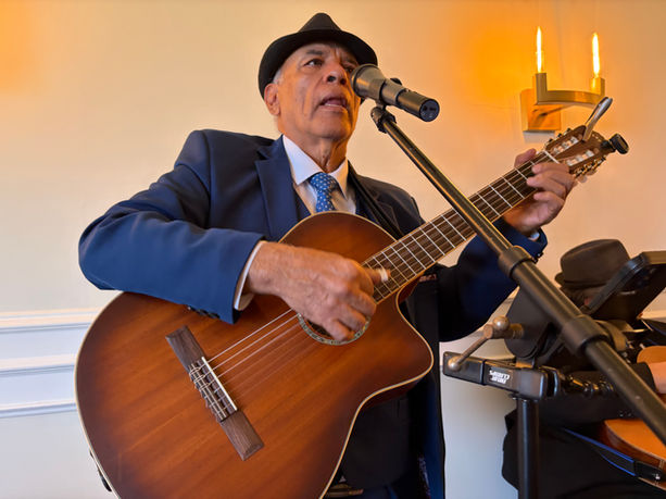Trio musician singing and playing acoustic guitar into a microphone during a live performance.