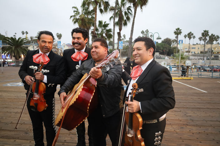 Mariachi musicians walking together outdoors with violin and guitars in traditional attire