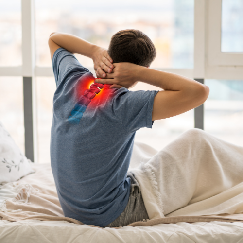 Man in blue shirt holding neck, sitting on bed in bright room. Red highlight indicates back pain. Mood suggests discomfort.