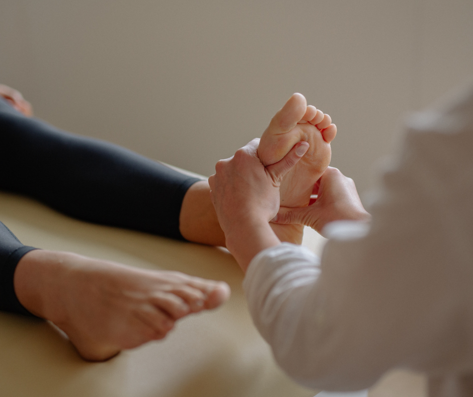 A person receiving a foot massage on a beige surface, wearing black leggings. The scene is calm and focused, with soft lighting.