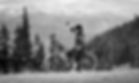 A mountain biker poses on their bike next to the trail with a view of the mountains in the background.