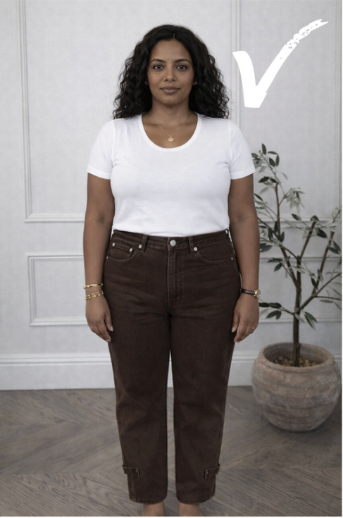 A rectangle woman stands wearing high rise brown barrel jeans